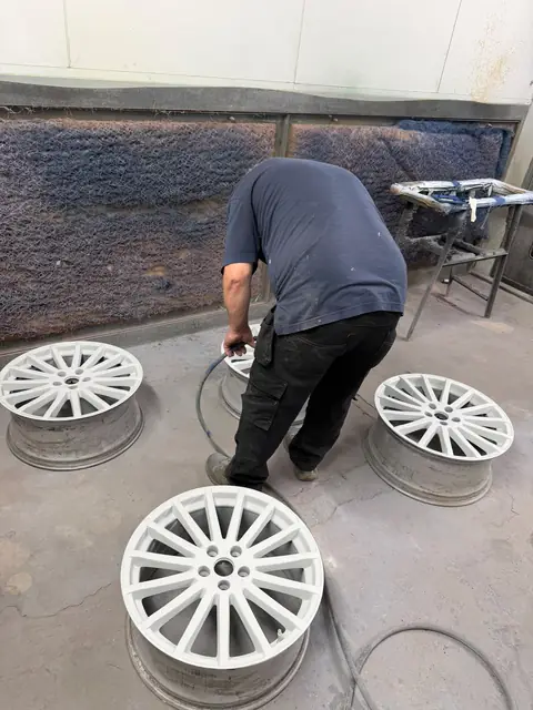 Four alloy wheels freshly painted white on the spray booth floor, with Mark working behind them