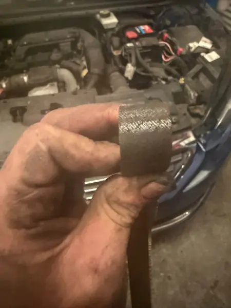 A worn timing belt part removed from a Peugeot 308 during a timing belt and water pump kit change, held over the engine bay