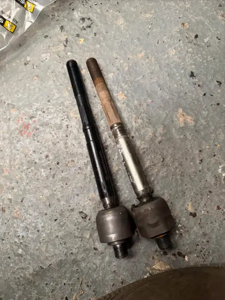 An old, rusty inner steering rack arm next to its new replacement from a Renault Megane